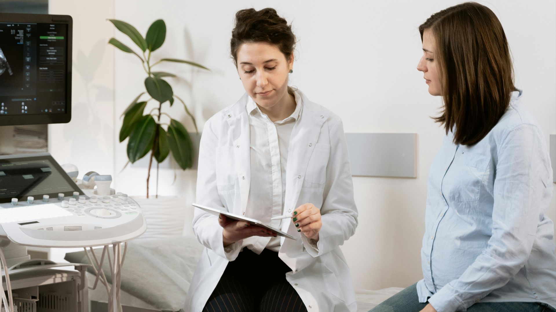 Doctor consulting pregnant woman with ultrasound machine in a medical clinic.