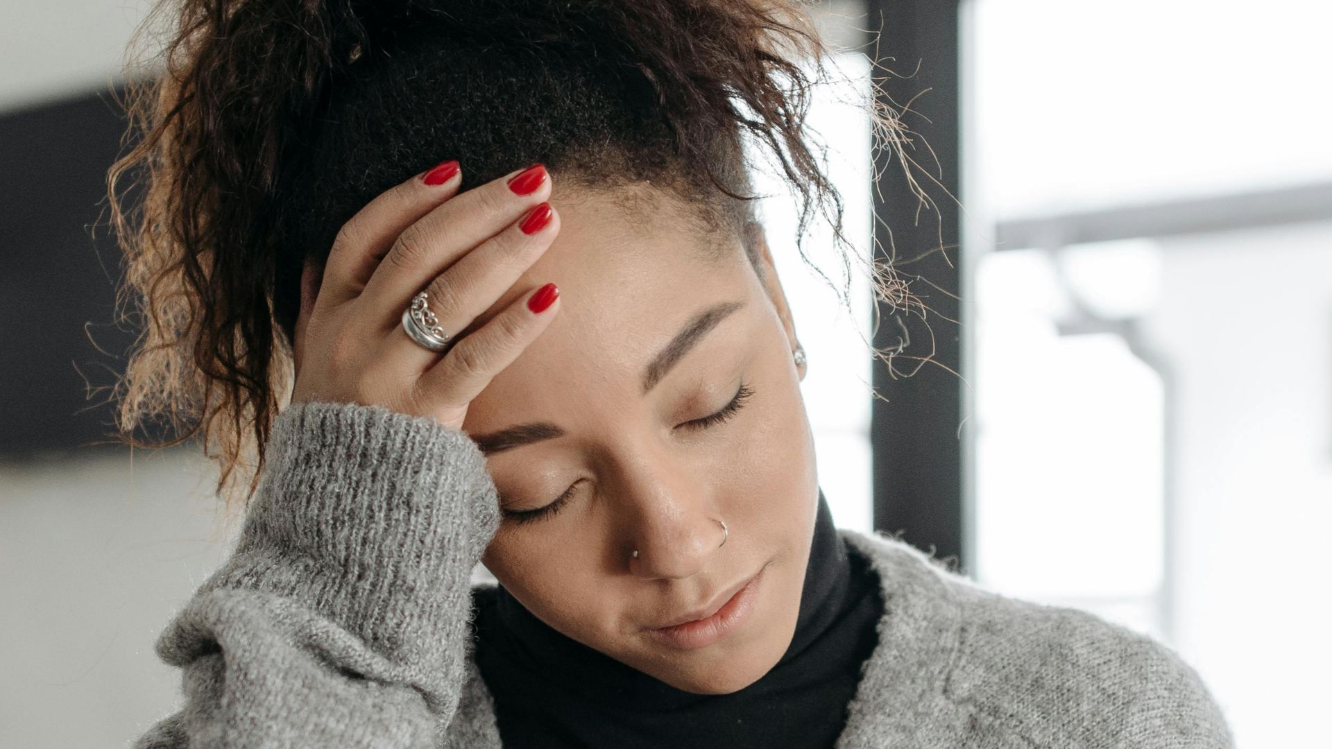 A young woman with a headache and malaise, wearing a cozy sweater indoors.