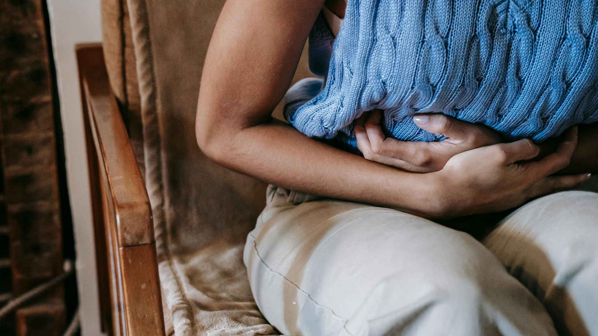 Crop unrecognizable female touching belly while having acute pain in stomach sitting on couch