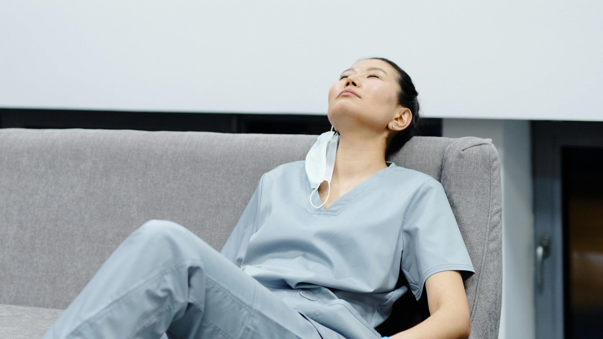 Nurse in scrubs takes a break, resting on a comfy hospital couch after a long shift.