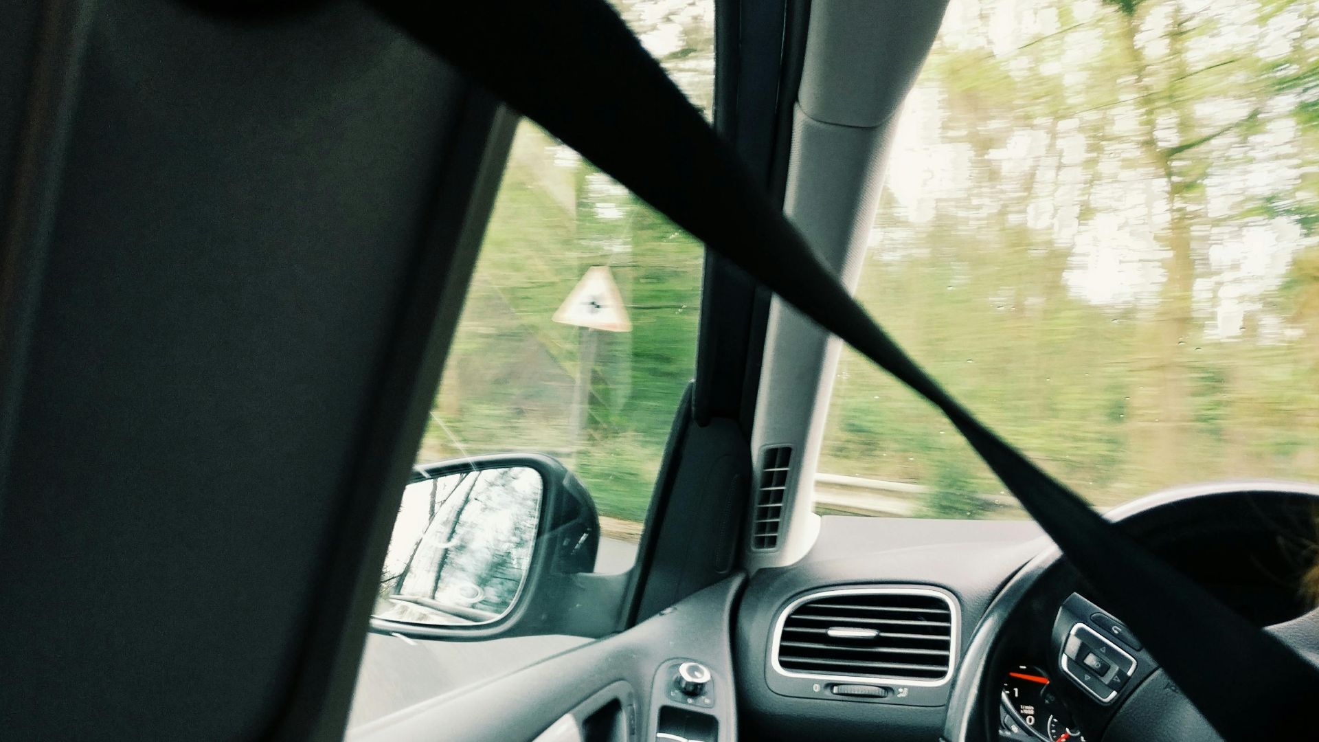 Interior car view with a driver on a scenic drive, showcasing modern design and safety features.