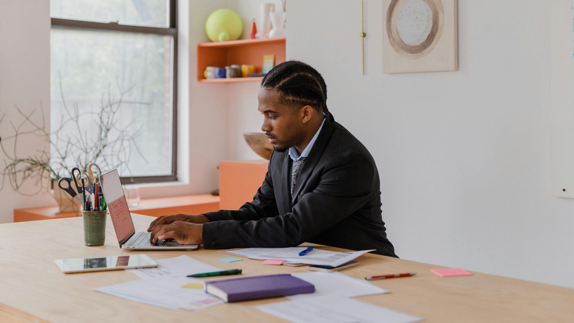 Professional businessman with braided hair working on a laptop at an office desk.