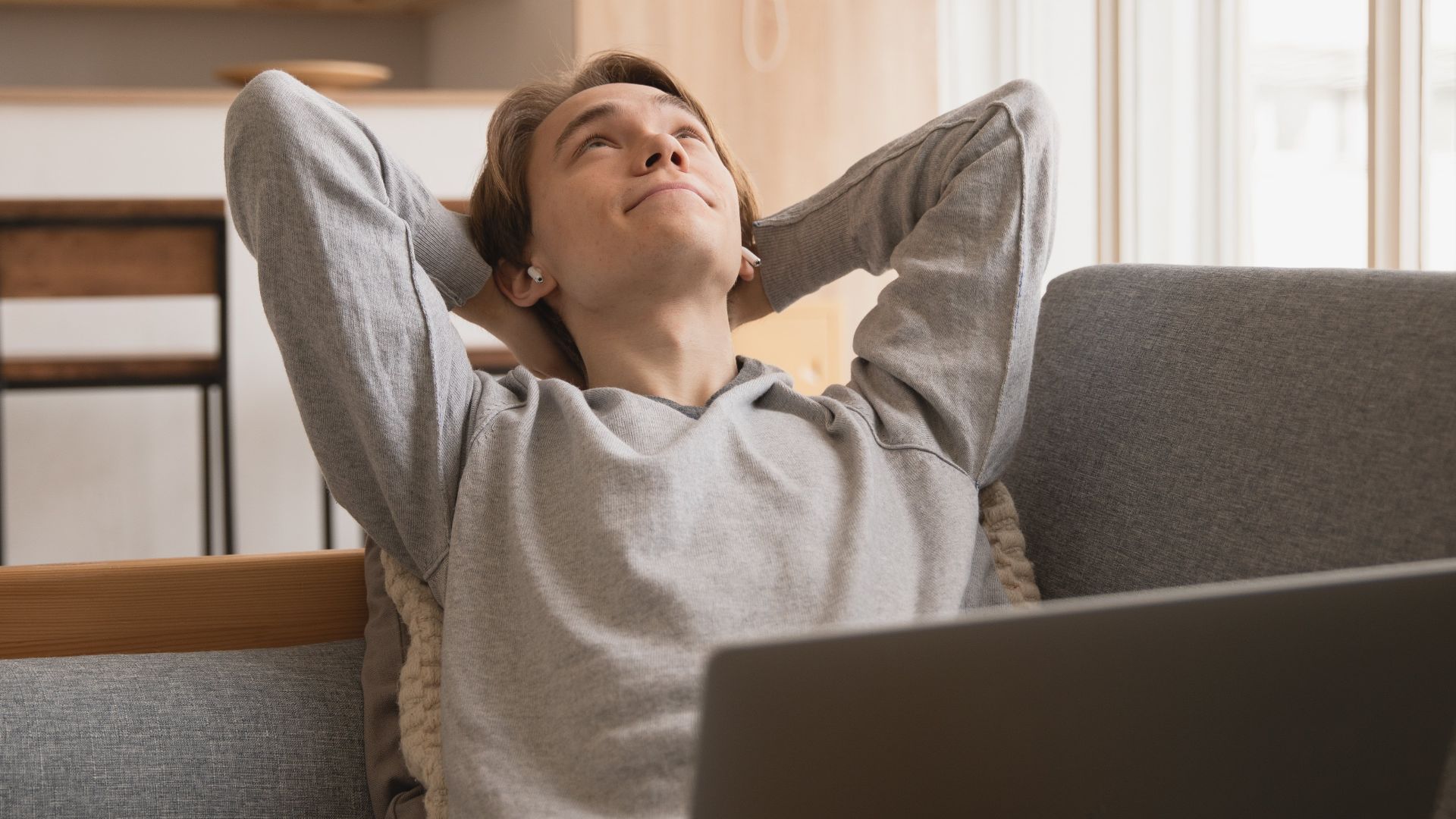 A young man relaxes on a sofa with a laptop, enjoying a peaceful moment indoors.