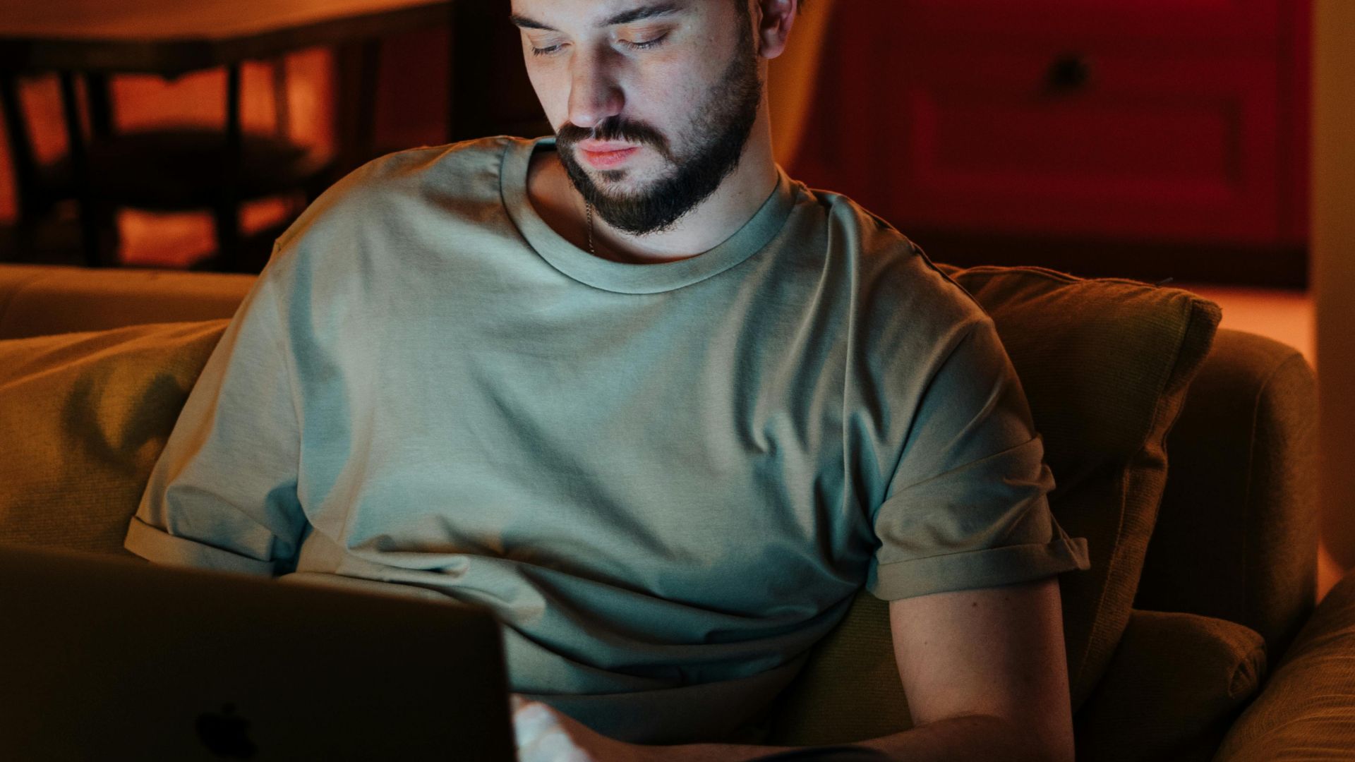 Man working on laptop in cozy home environment with warm lighting.