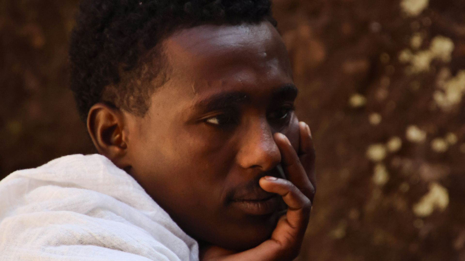 A man in a white robe resting his chin.