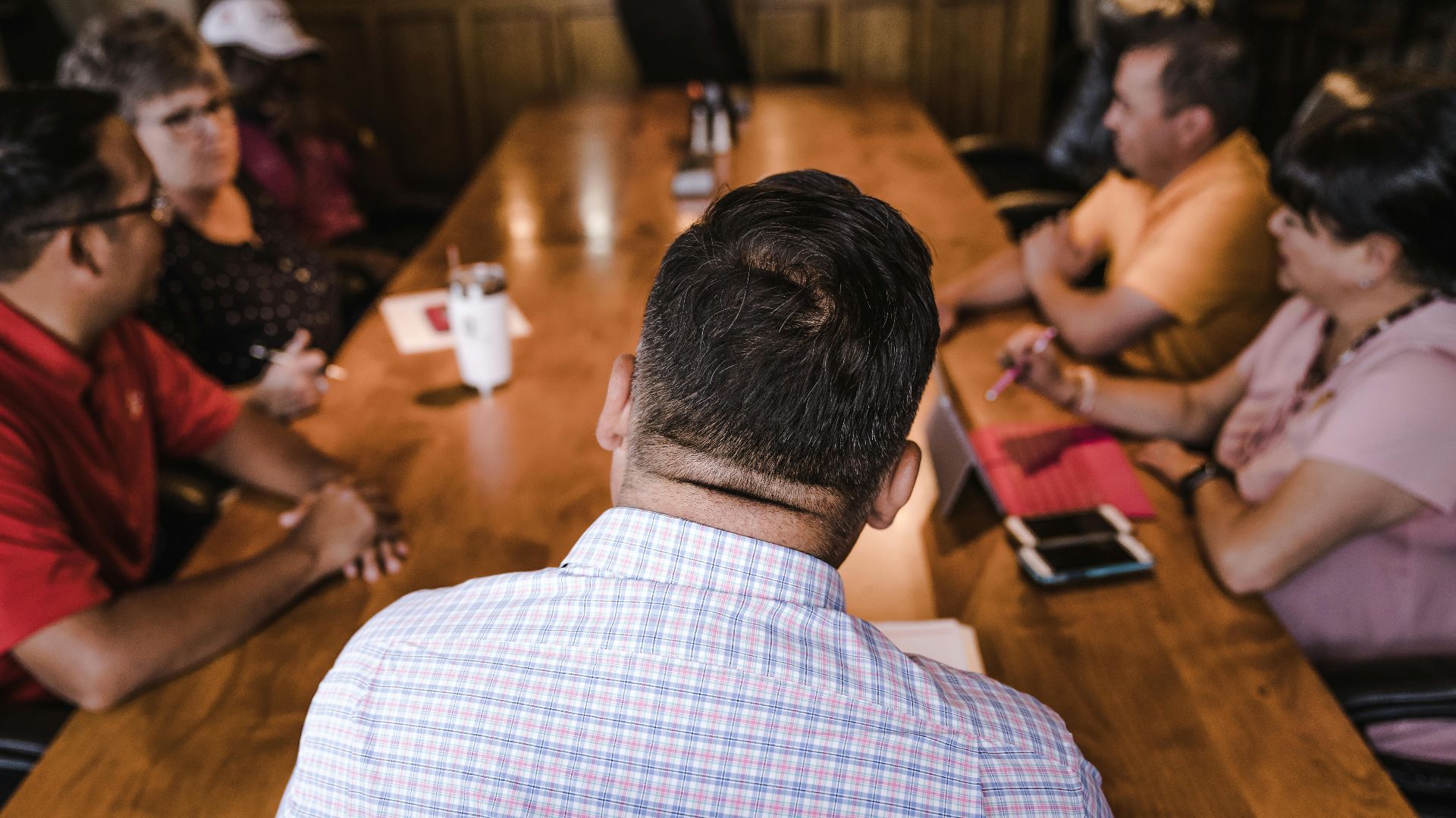 A business meeting with a diverse team discussing around a wooden table in an office setting.