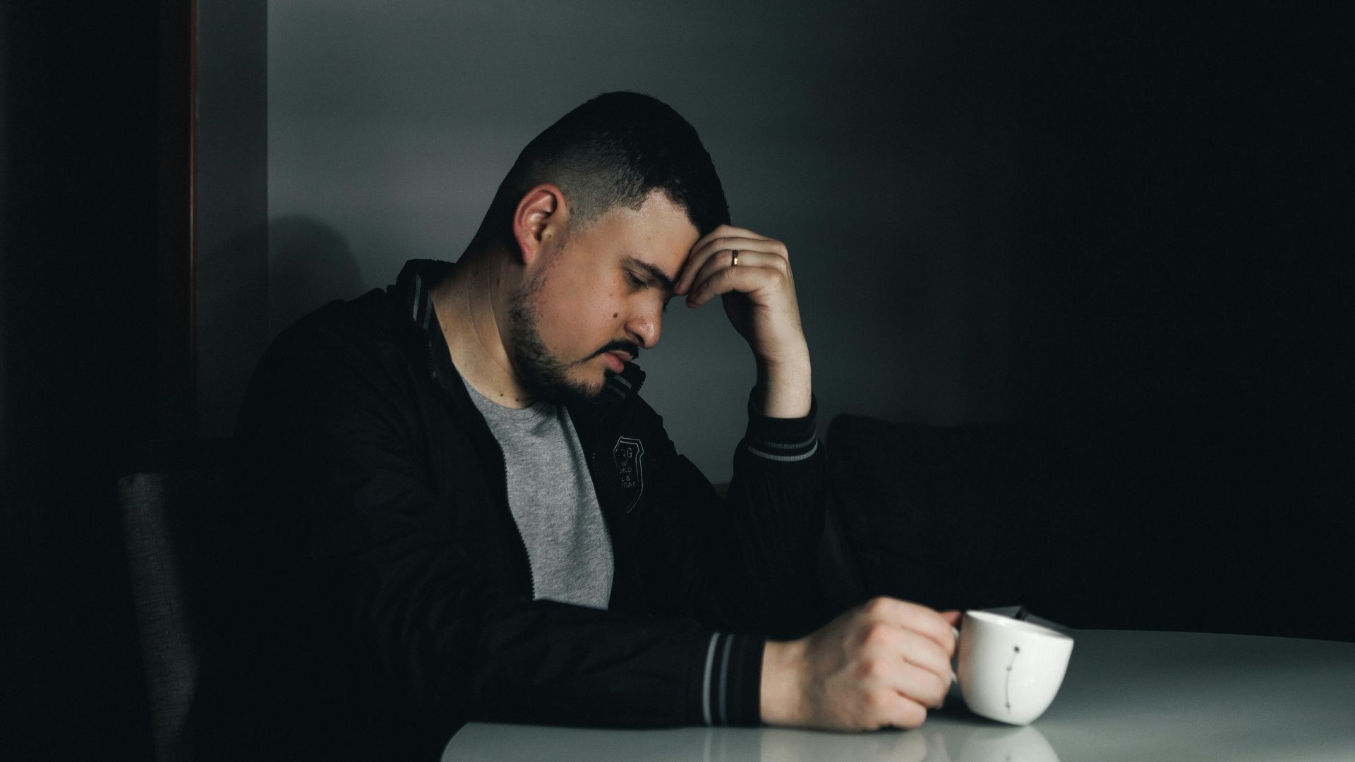 A thoughtful man in a dark room holding a coffee cup, depicting a moody morning scene.