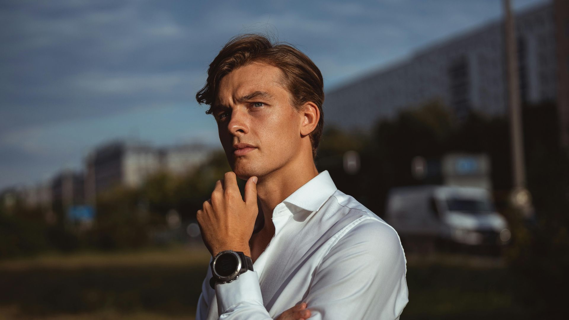 Portrait of a young man in white shirt outdoors, exuding a contemplative mood against an urban backdrop.