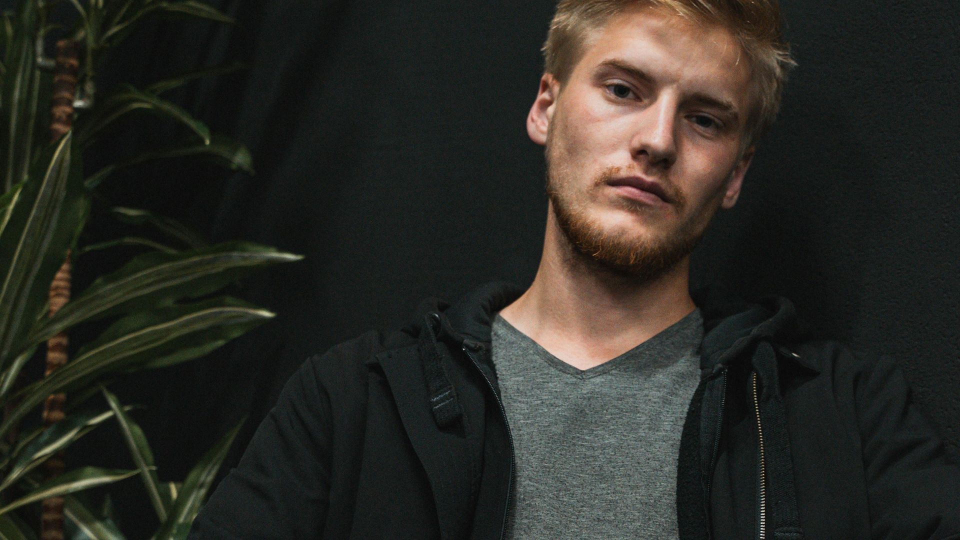 Caucasian man in casual attire posing while sitting with a plant backdrop.