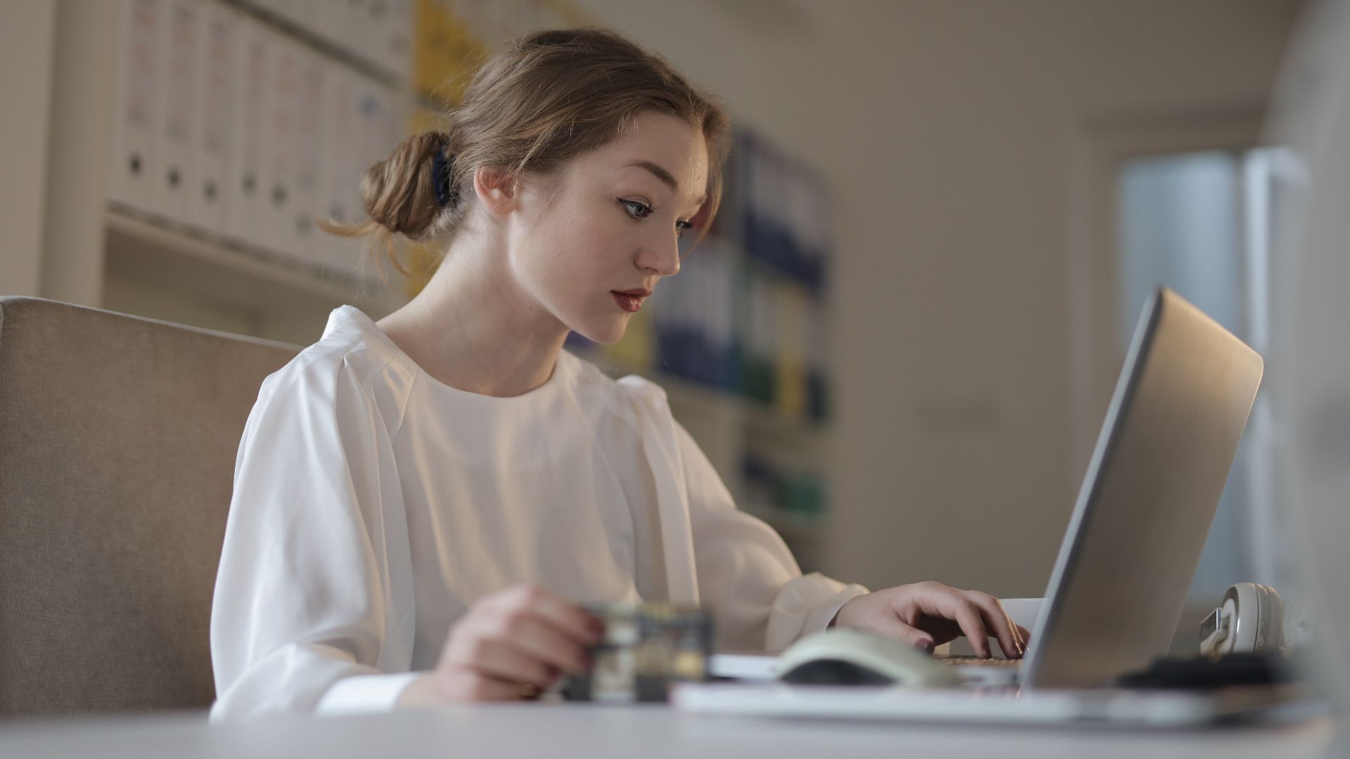 Focused young woman working remotely on a laptop in a modern office.