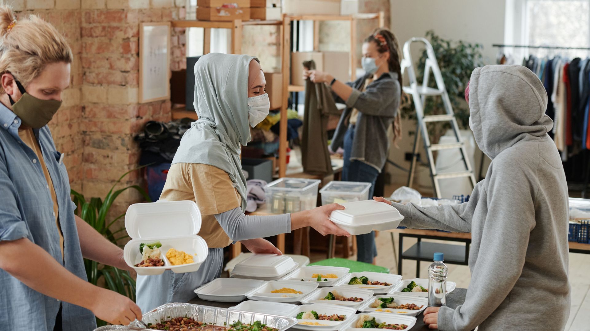 Volunteers wearing face masks distribute food in takeaway boxes at a community charity event.