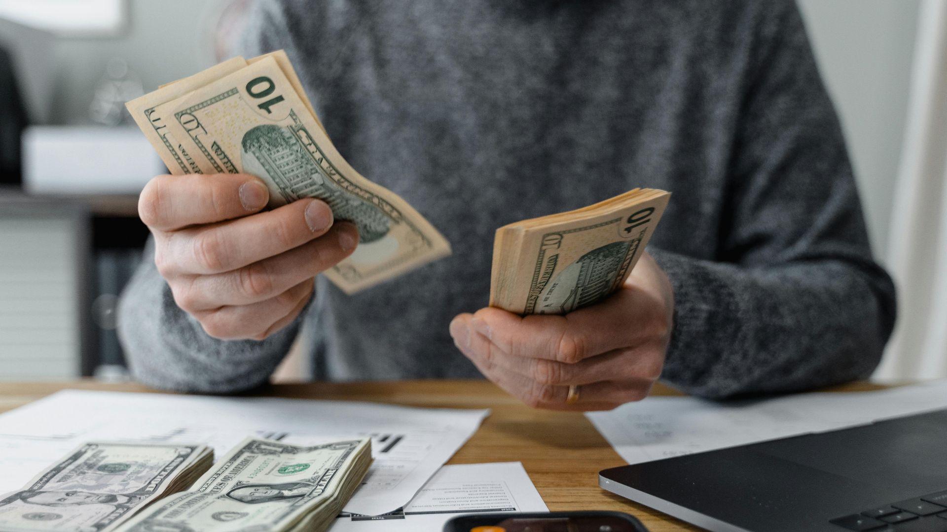 Close-up of person counting cash with a calculator and paperwork on a desk.