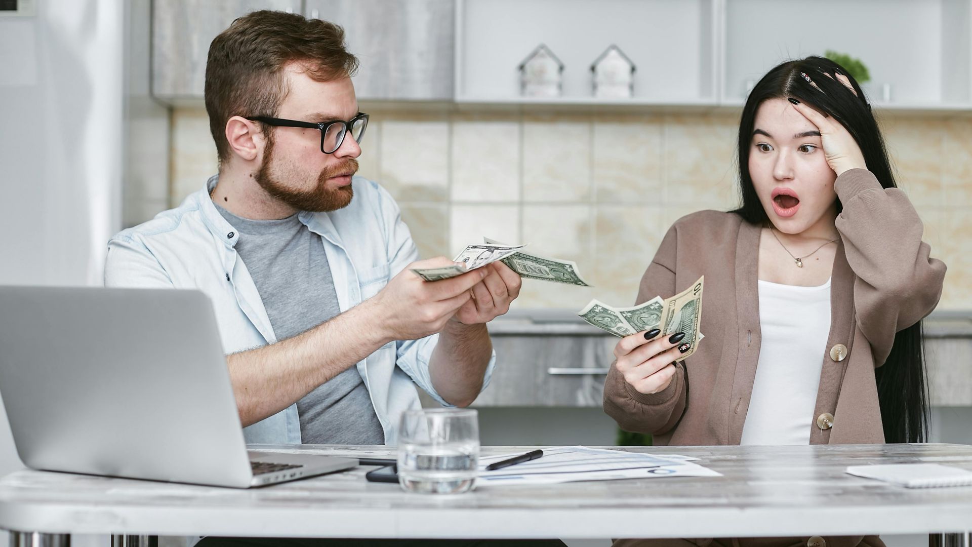 A shocked couple sitting at a table counting cash, illustrating financial surprise.