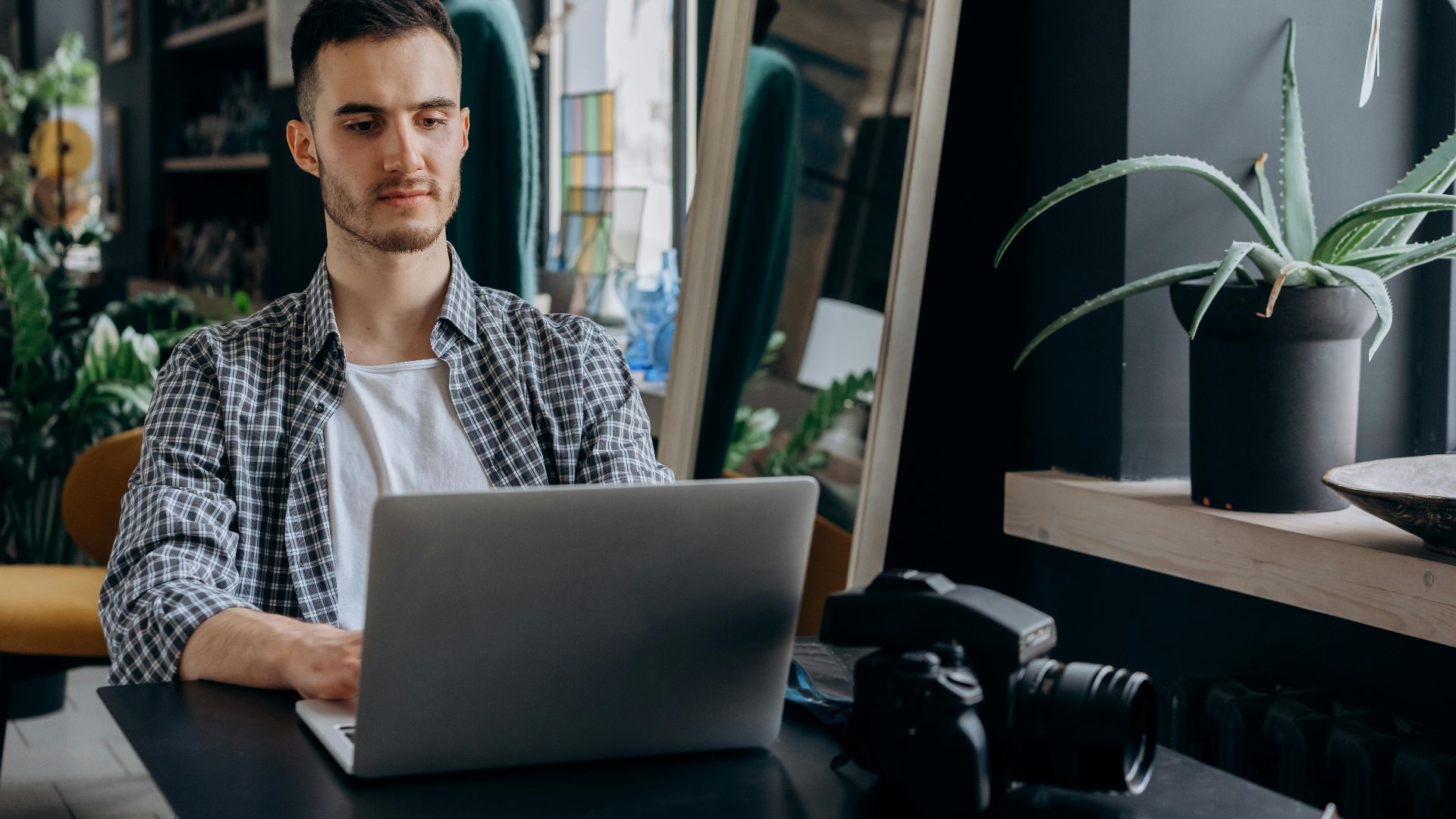 Man in plaid shirt working on a laptop in a modern home office setting.