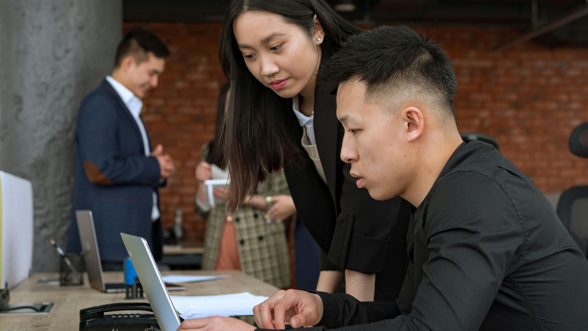 Professionals working together in a modern office setting around a laptop.