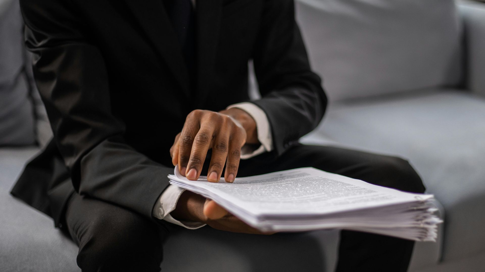 Close-up of a businessman in a suit reviewing documents while seated on a sofa indoors.