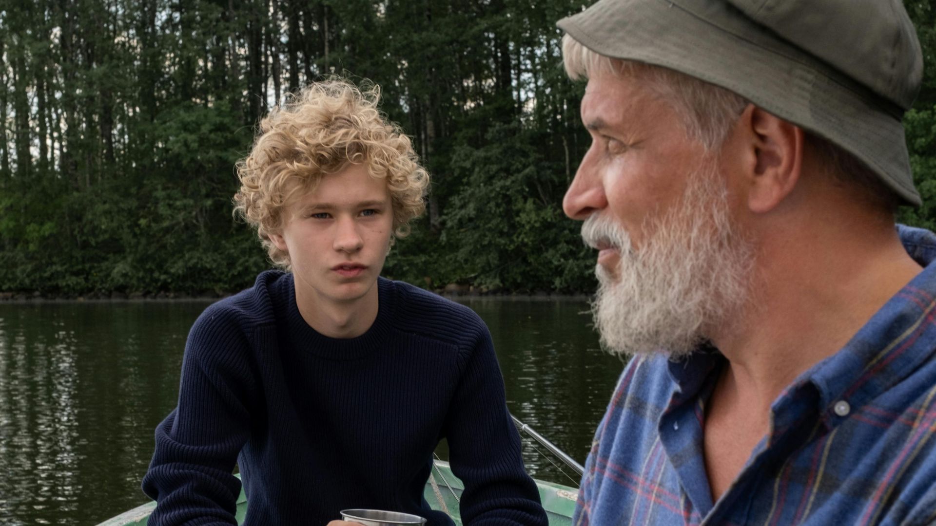 An elderly man and a boy sitting in a boat on a serene lake, enjoying a quiet moment together.
