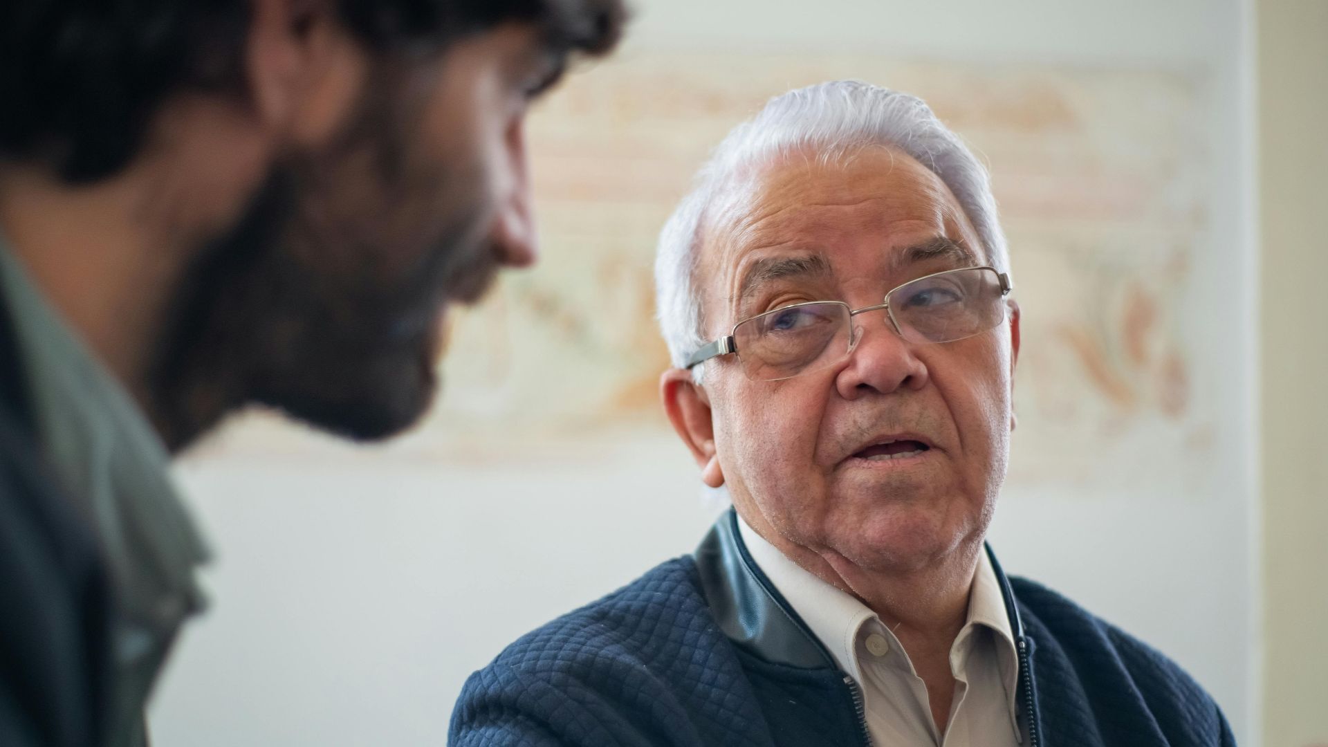 Elderly man with eyeglasses in a thoughtful discussion in Portugal indoors.