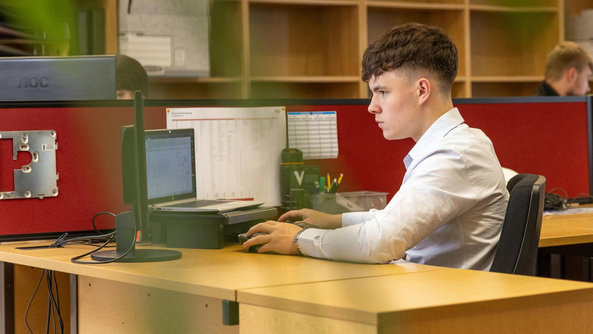 A focused young man typing on a computer in a contemporary office environment.