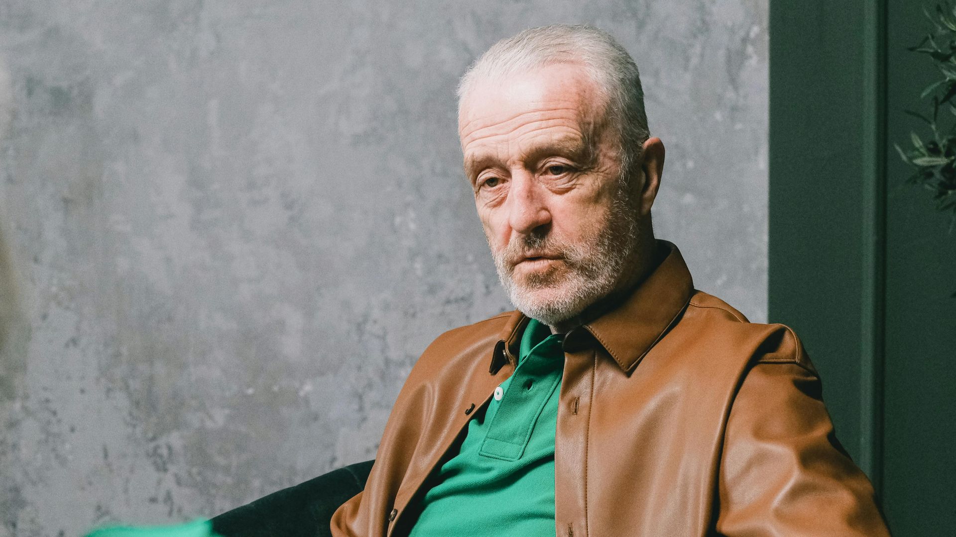 Elderly man in brown leather jacket during a conversation indoors.