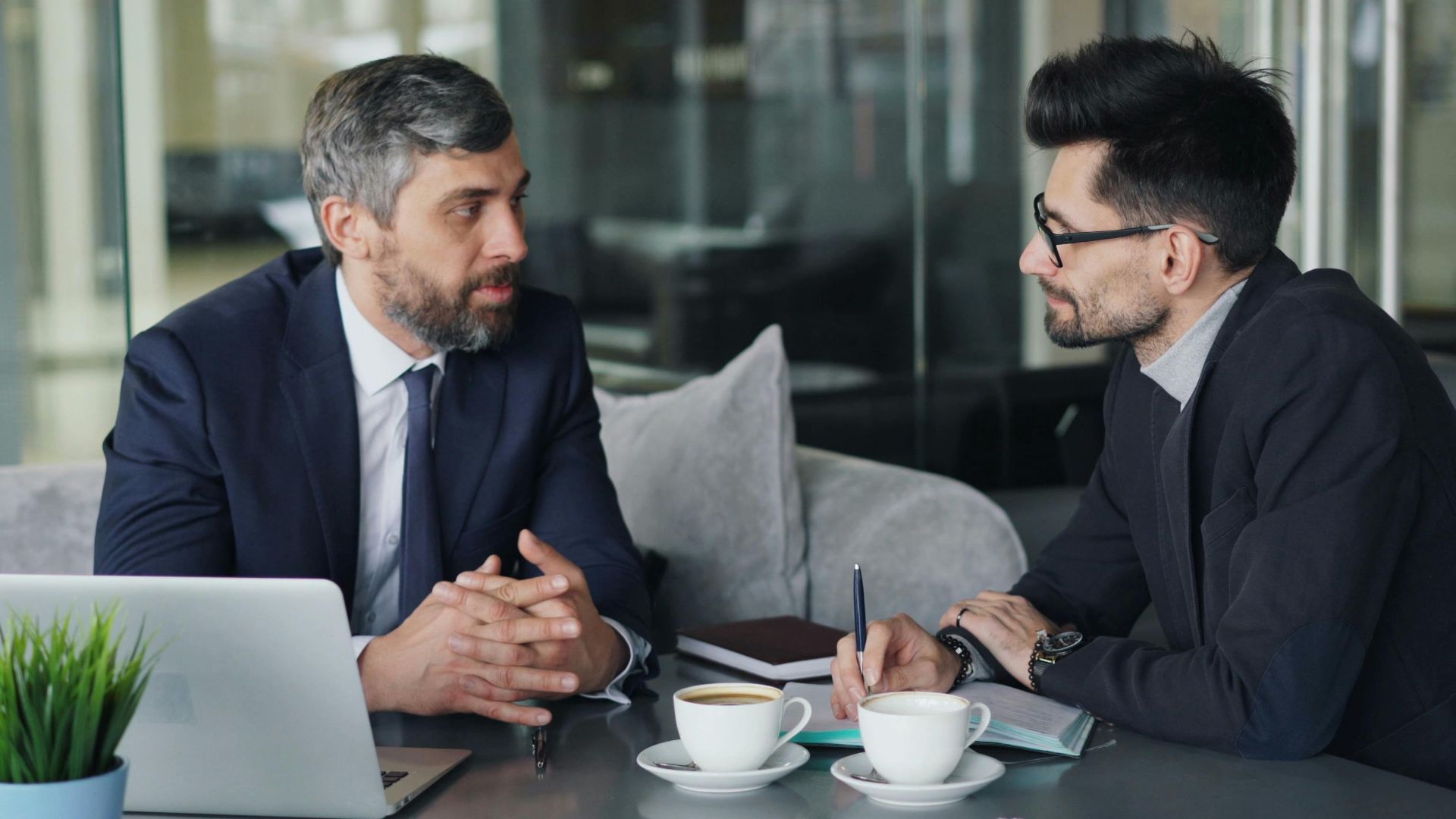 Two businessmen having a meeting with laptops, papers, and coffee at a modern office.