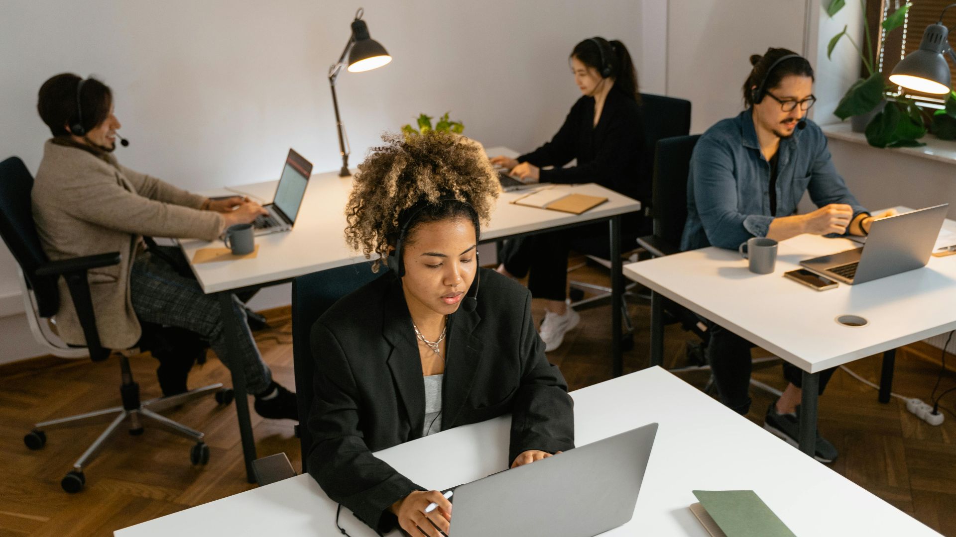 Diverse team of call center agents working at computers in an office setting, focused on tasks.