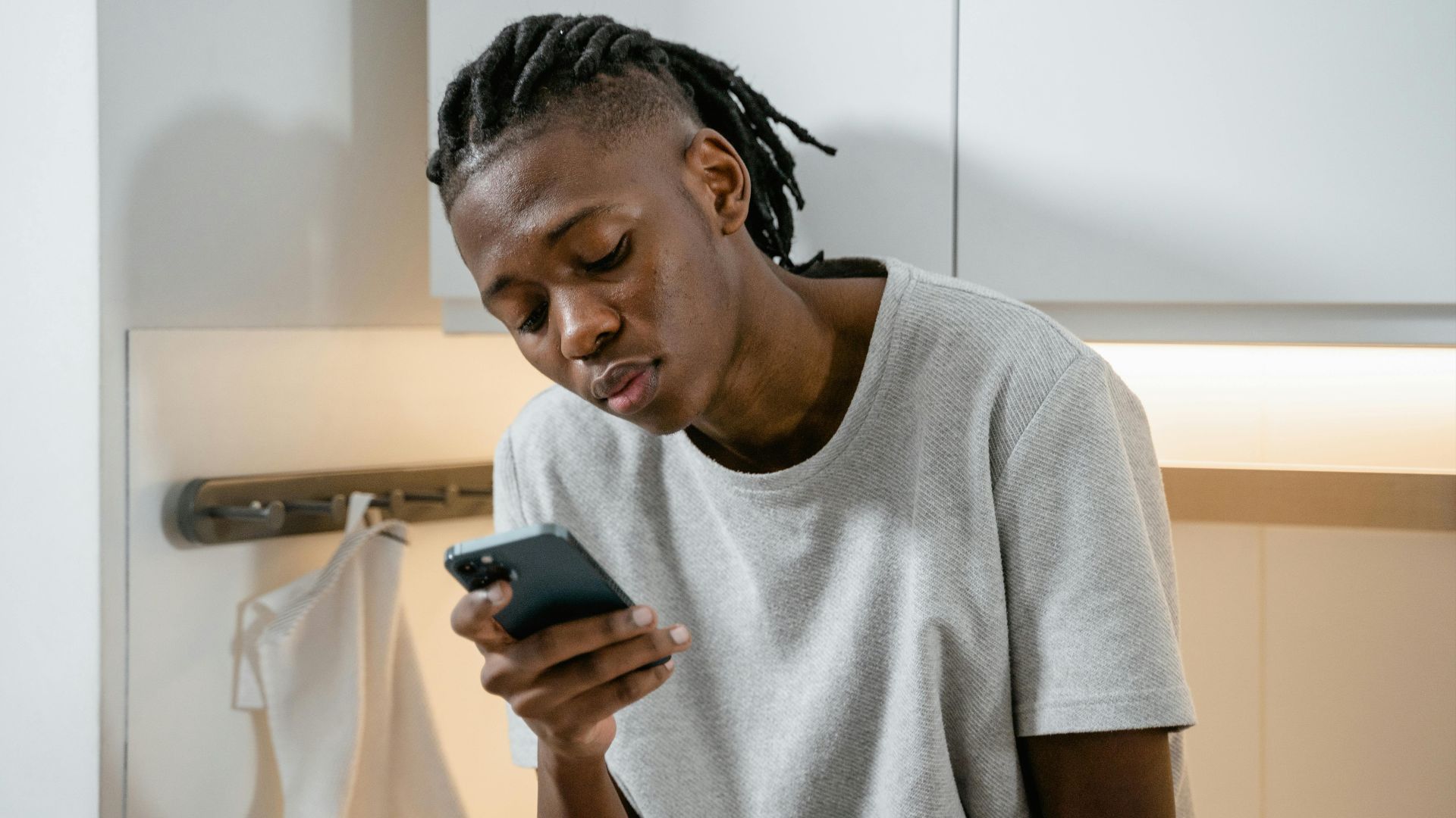 Focused individual texting on smartphone in modern kitchen environment.