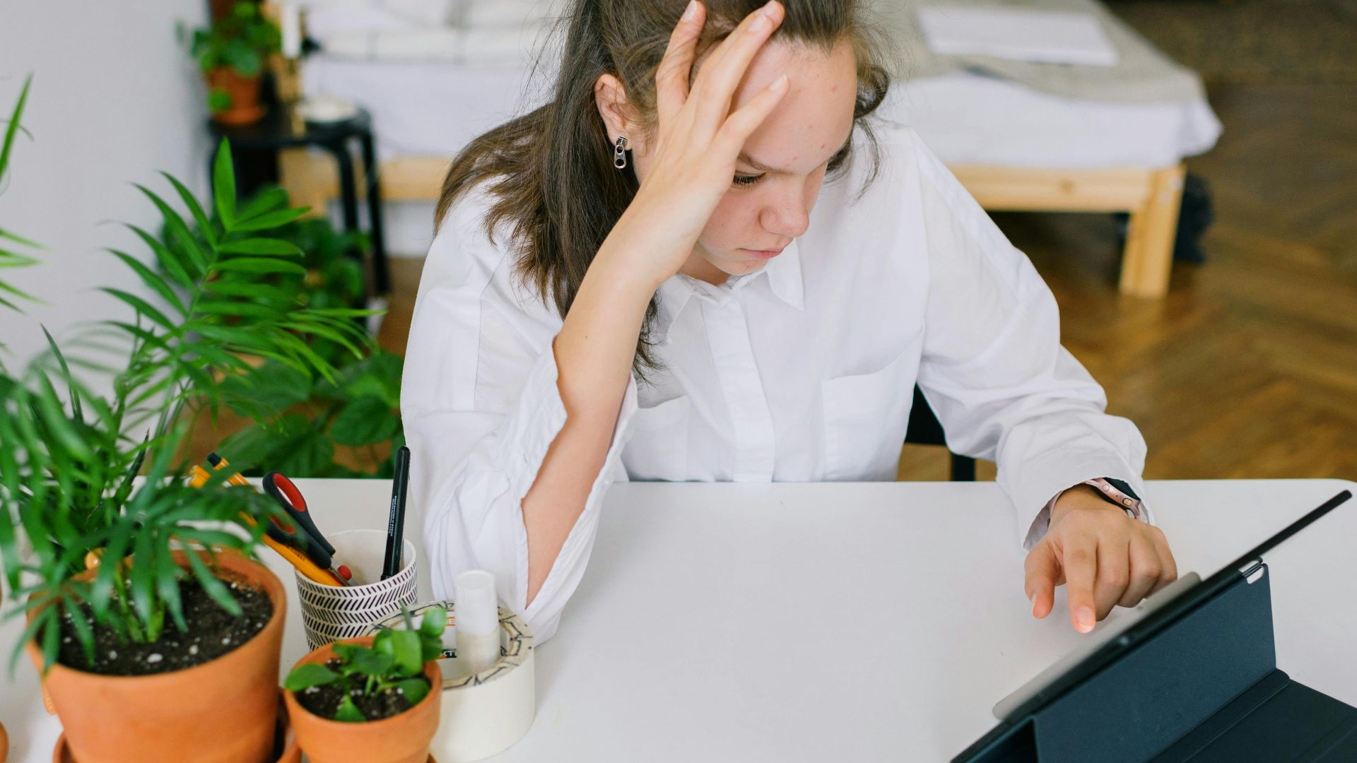 Young woman in white shirt using tablet in home office with plants.