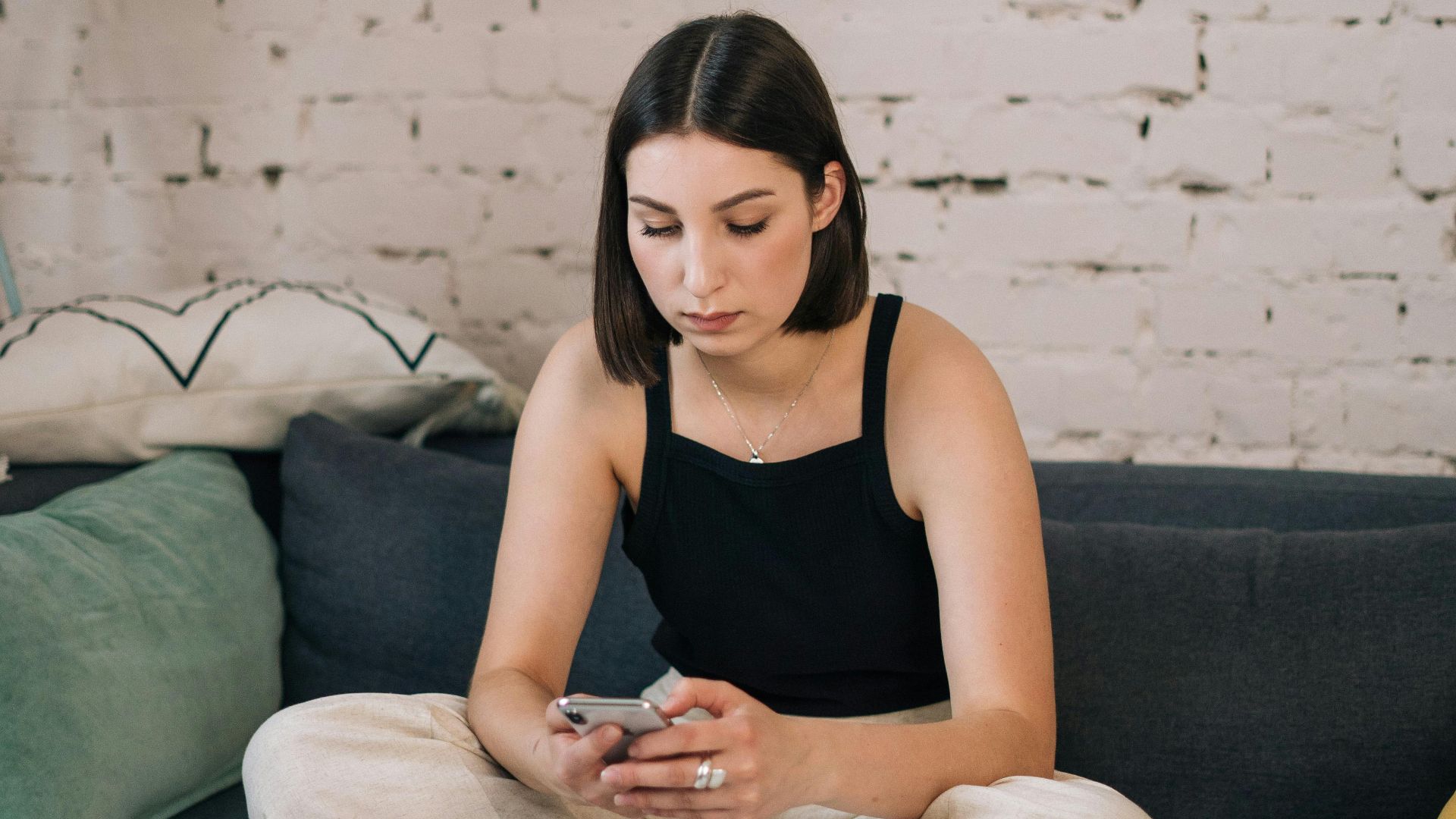 Young woman sitting comfortably on a sofa using smartphone in a chic living room setting.