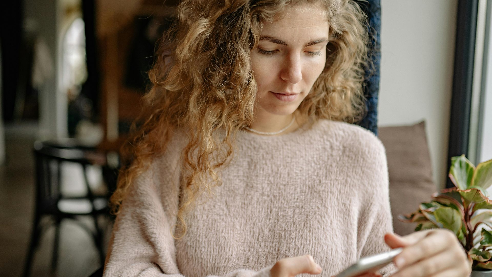 A woman in a cozy sweater using a smartphone in a relaxed indoor environment.