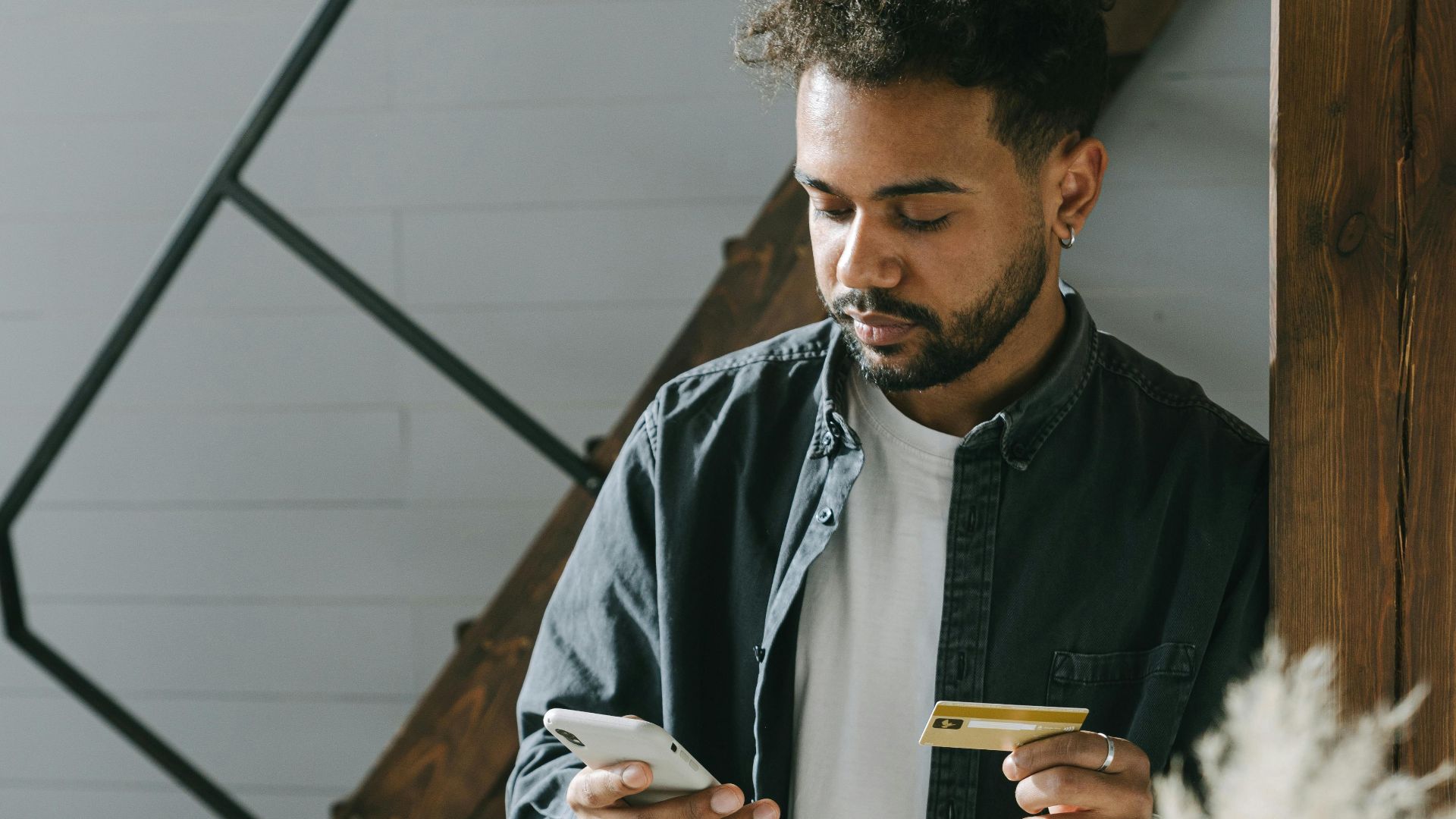 Man using smartphone and card for an online payment in a modern indoor setting.