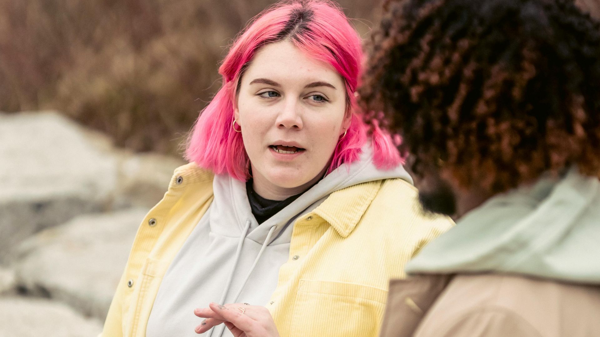 Plump woman with pink hair having conversation with faceless African American man while sitting on stones with cans of soda