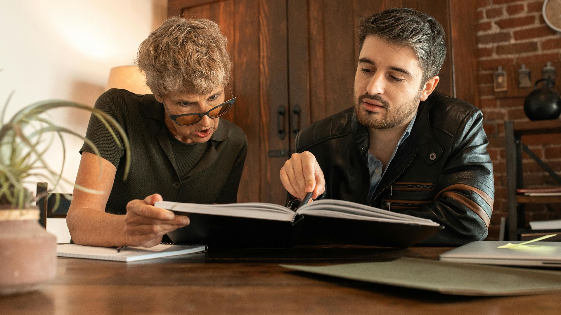 An elderly woman and a man study together in a cozy indoor environment.