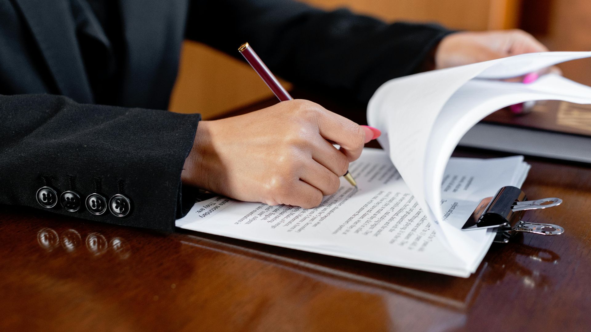 Close-up of a woman signing legal documents with a pen in an office setting.