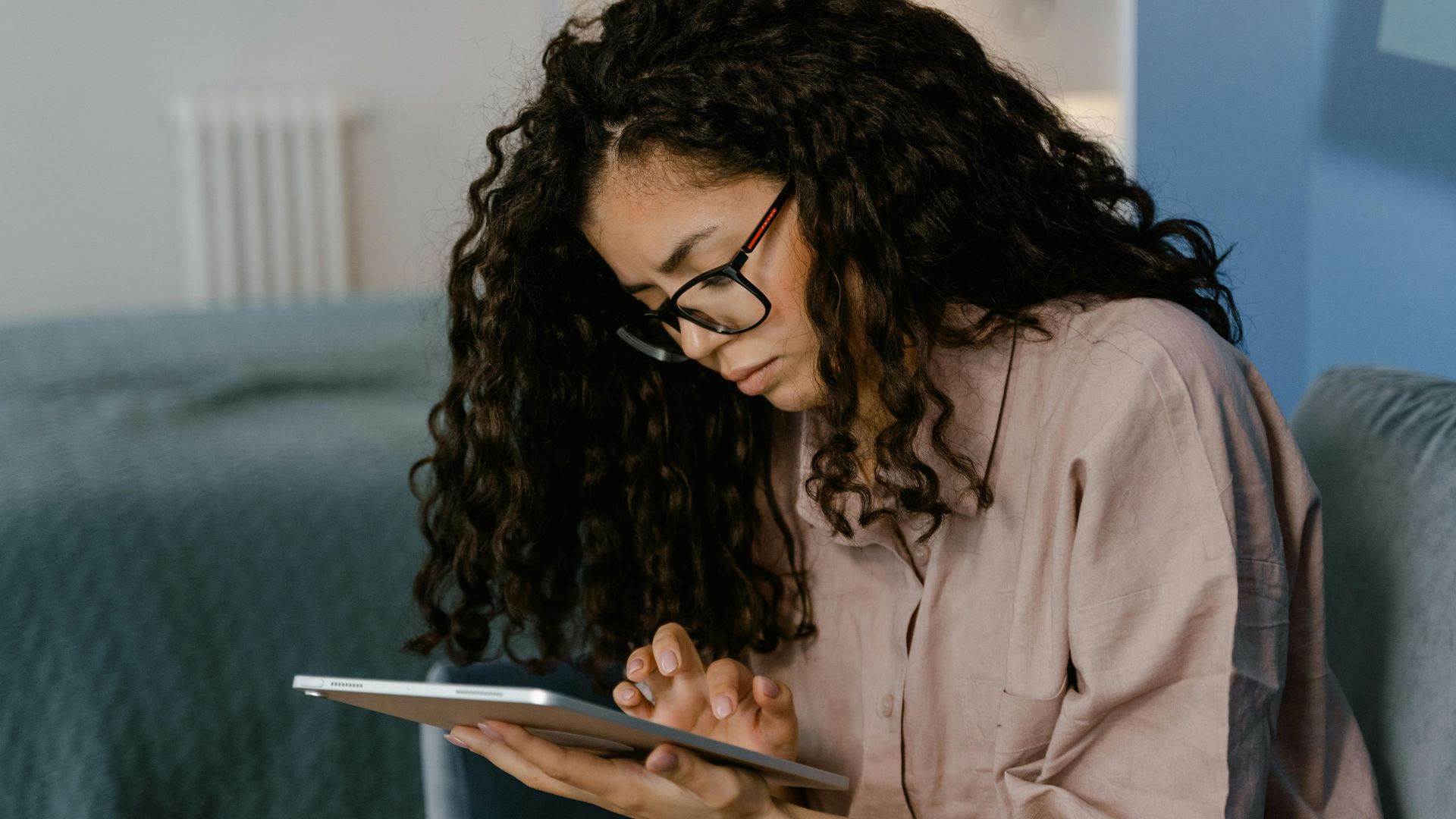 Young woman with glasses using a tablet indoors, focused on the device.