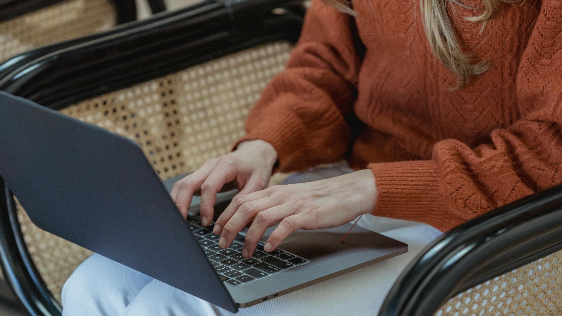 High angle of crop unrecognizable female remote employee sitting in armchair and typing on netbook while working online on startup