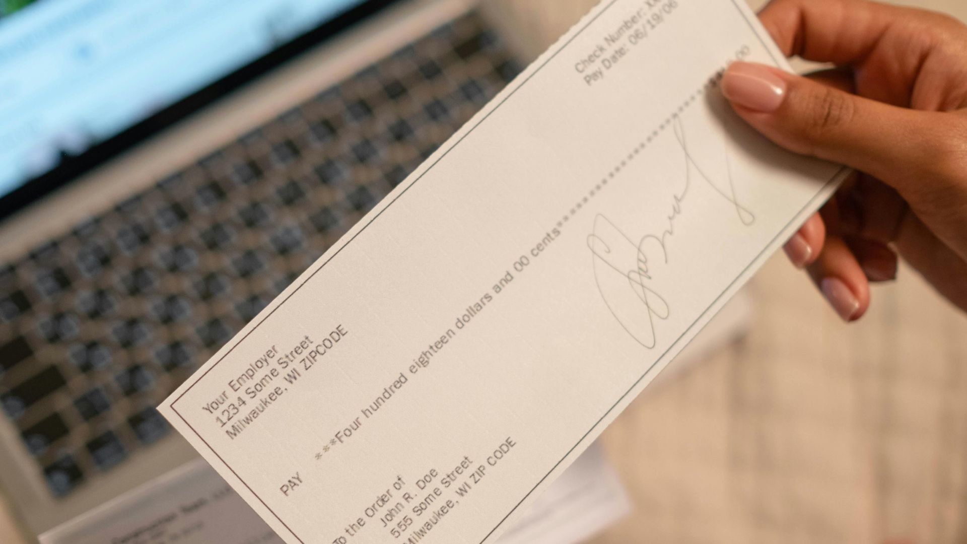 Individual holding a cheque over laptop, signifying online banking or financial transaction.