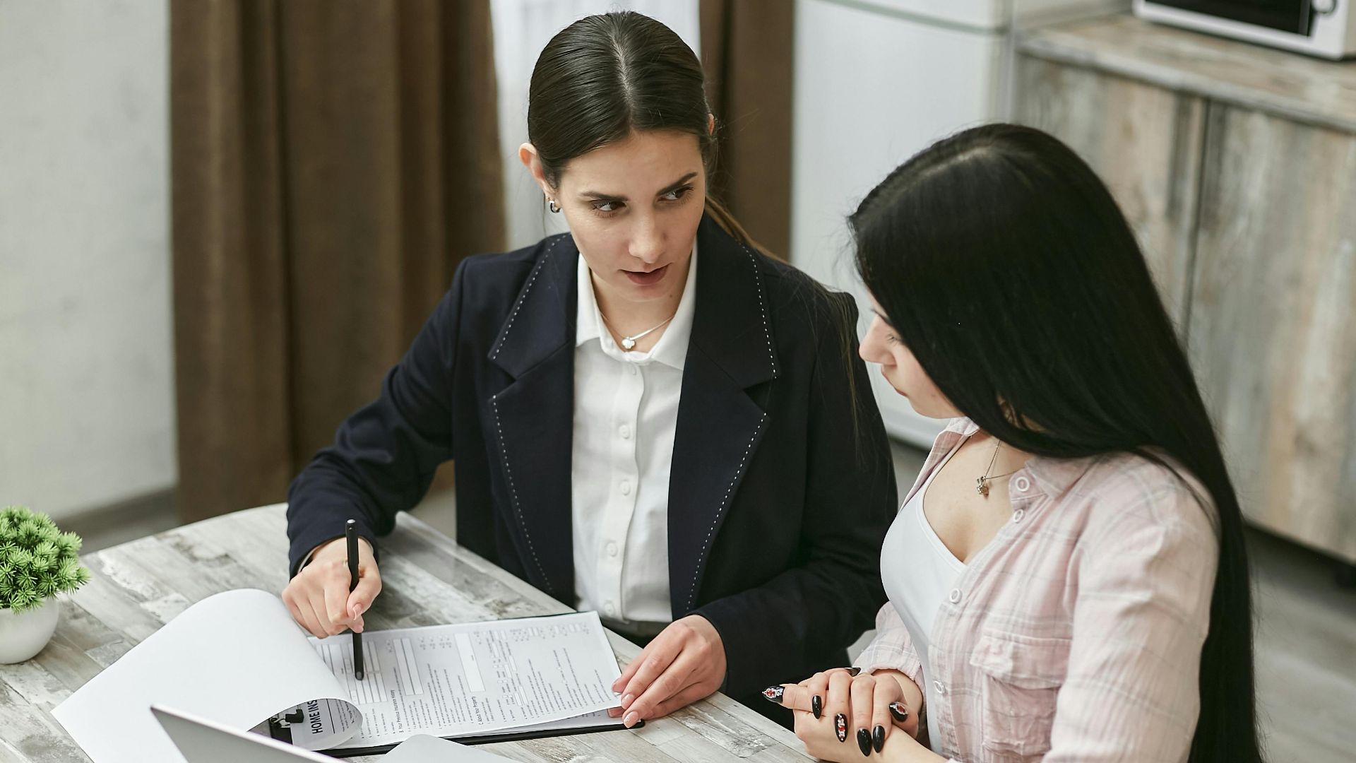 Two businesswomen engaged in a contract discussion at an office table.