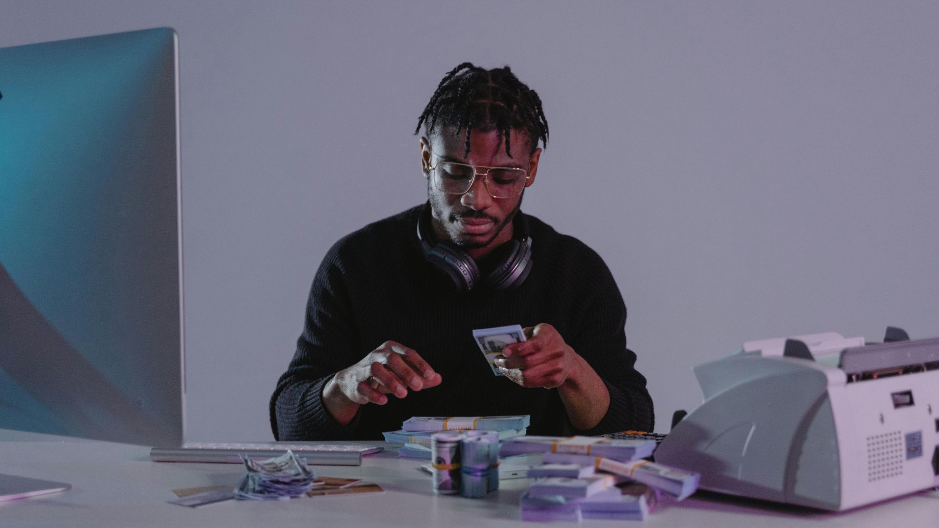 Focused man counting cash at an office desk with a computer and cash counting machine.