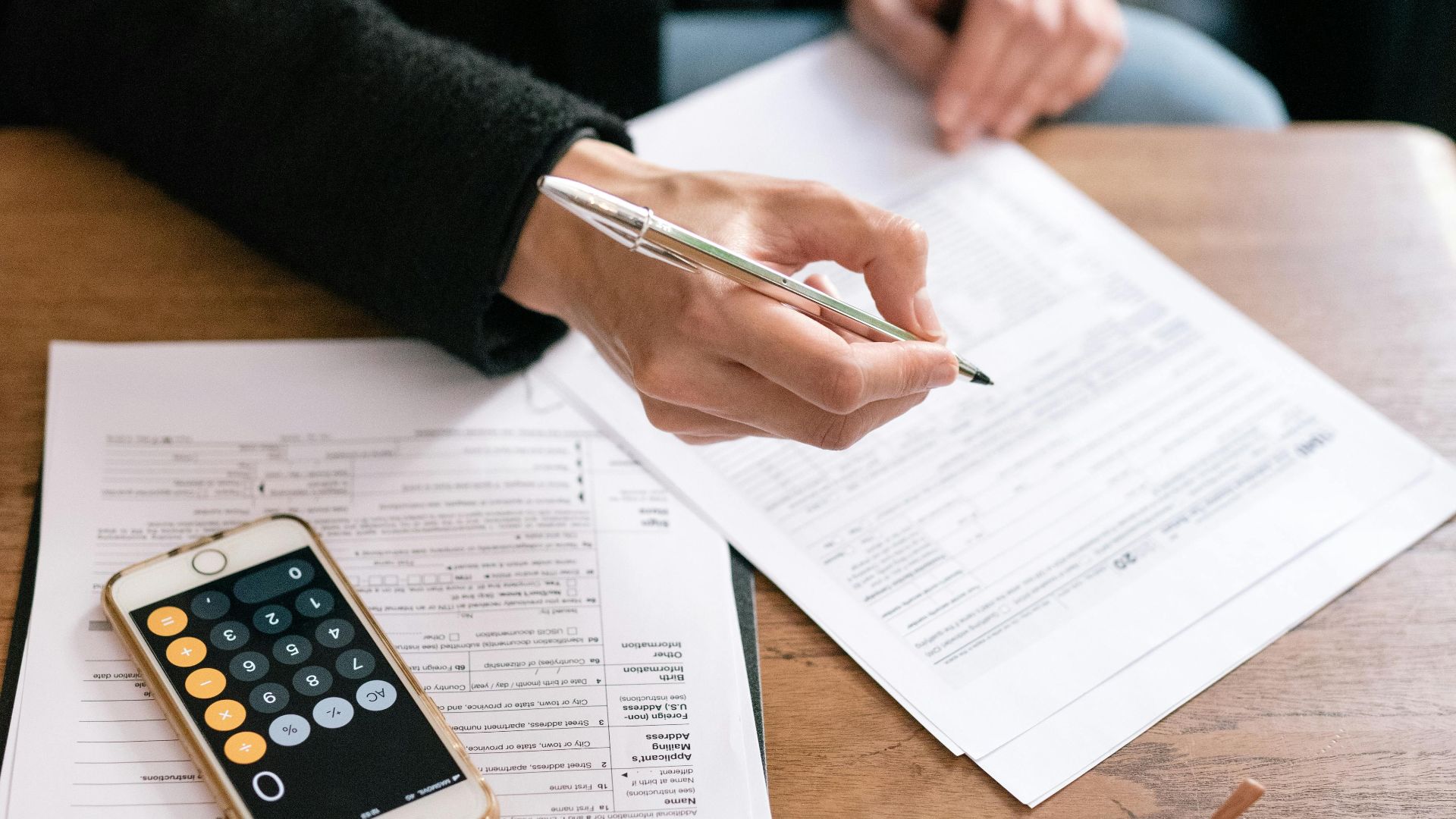 A woman reviewing financial documents with a calculator and glasses on a table.