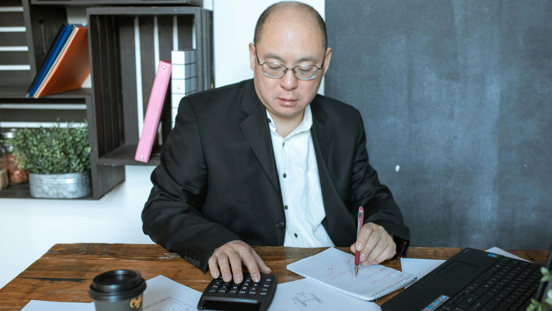 Asian businessman working with calculator and notes at his desk in a modern office space.