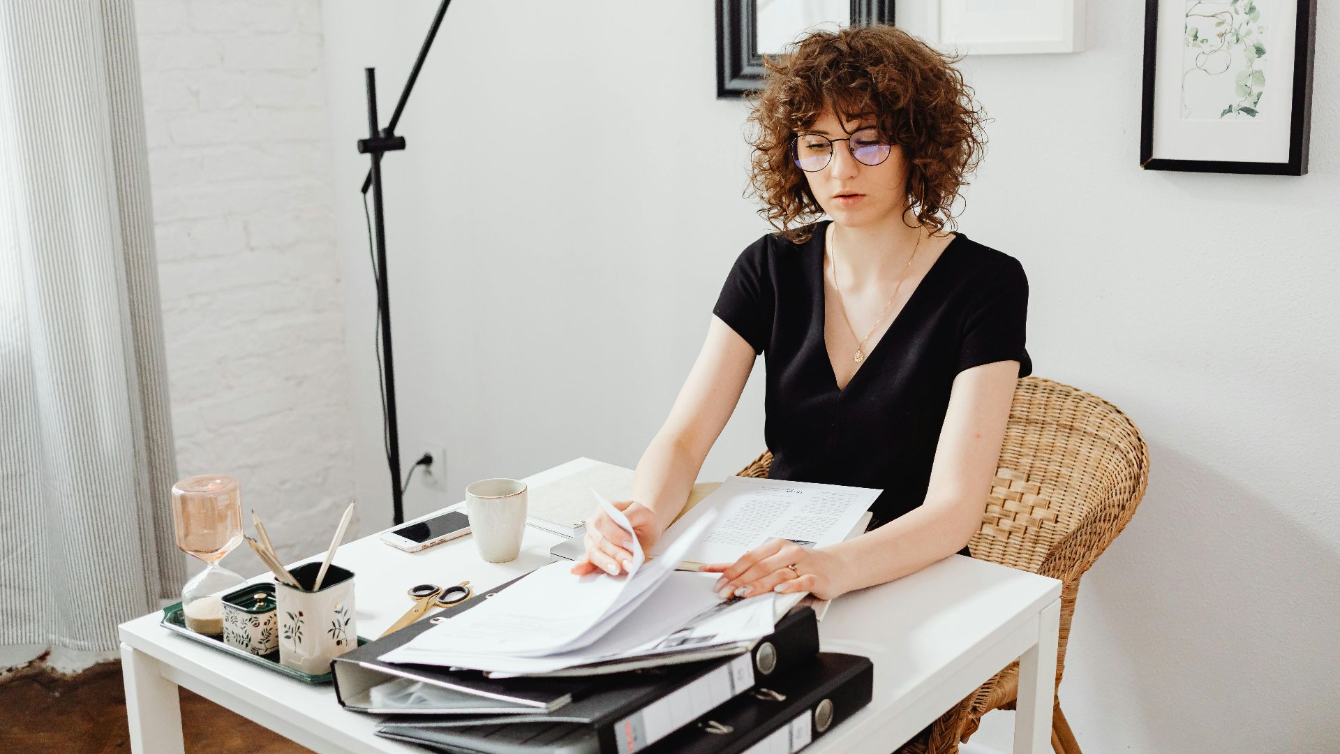 Woman with curly hair and eyeglasses working at a desk in a modern home office.