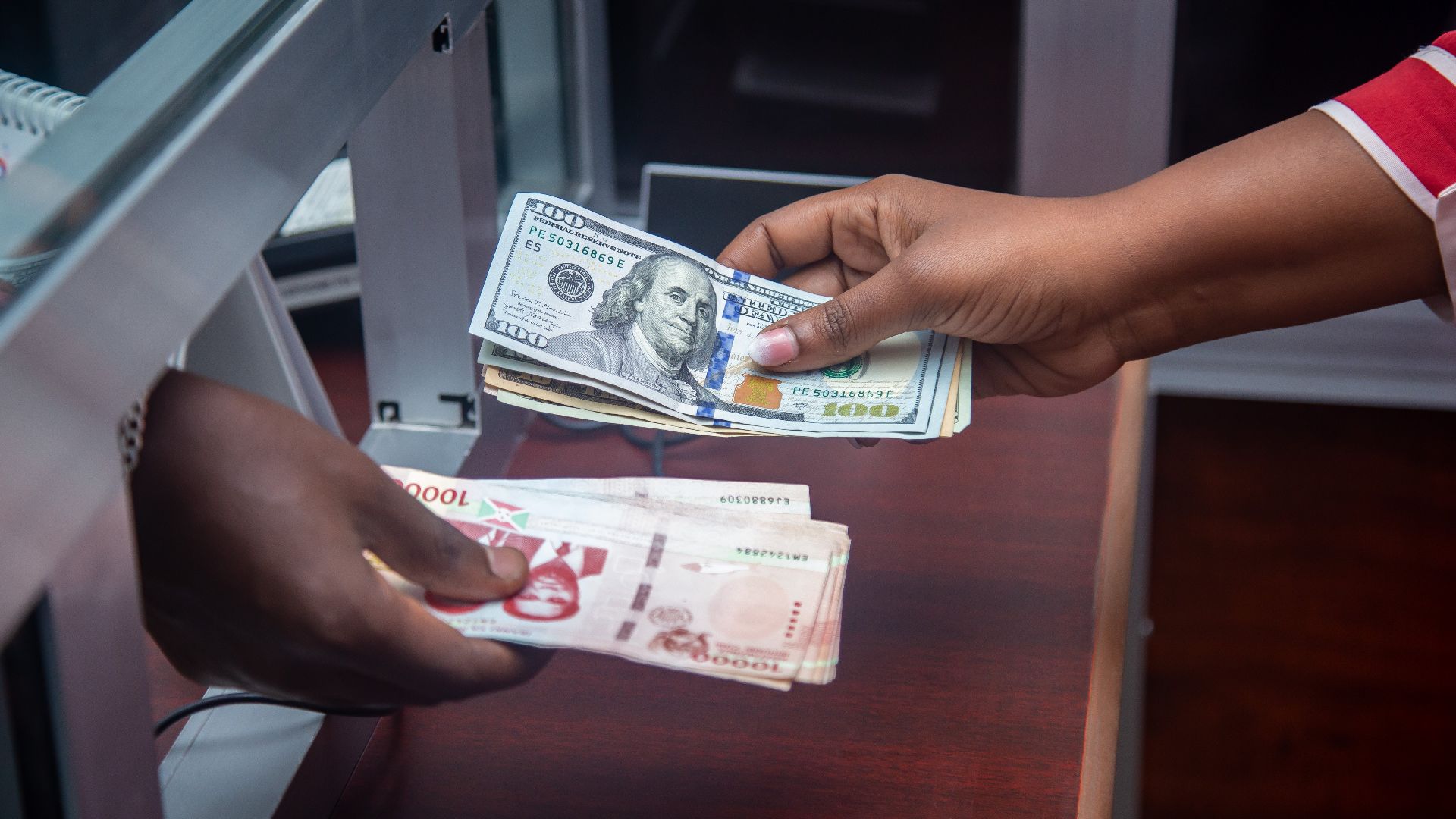 Hands exchanging US and local currency at a bank counter, signifying international finance.