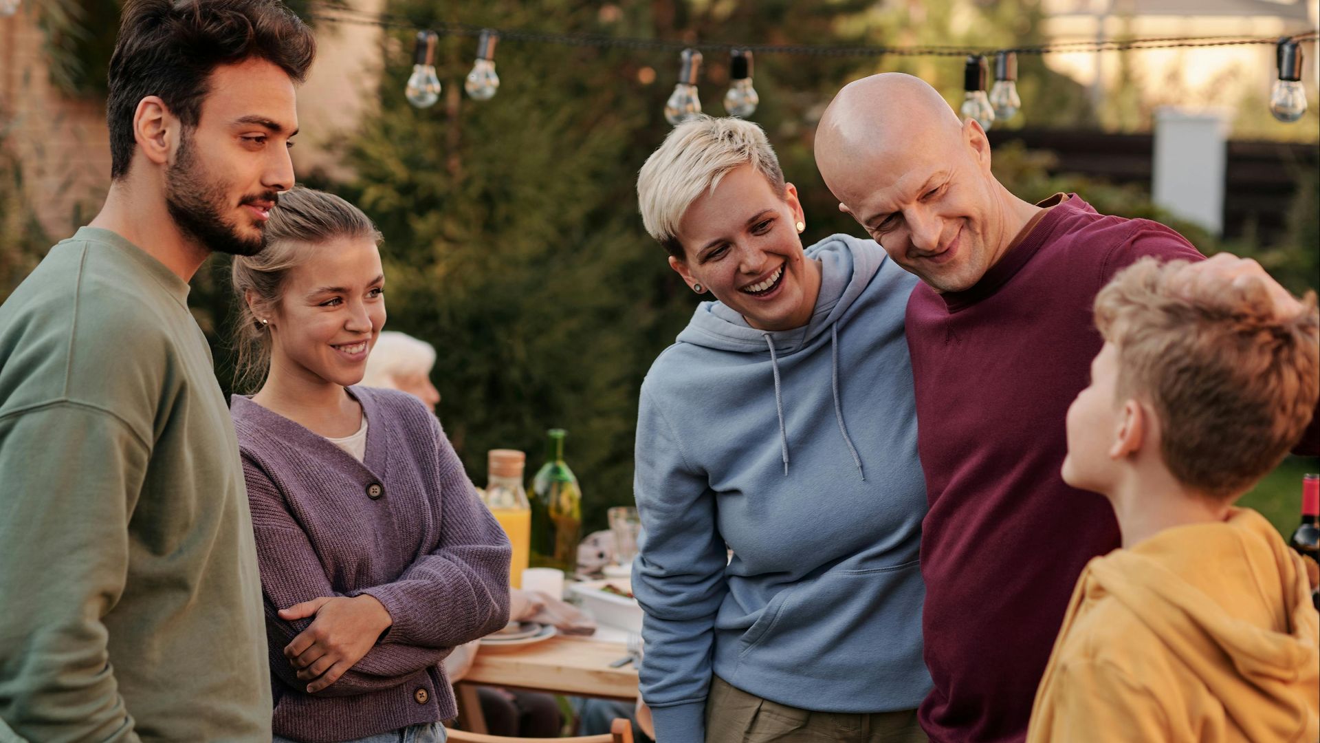 Group of family members smiling and chatting in a backyard setting during a summer evening.