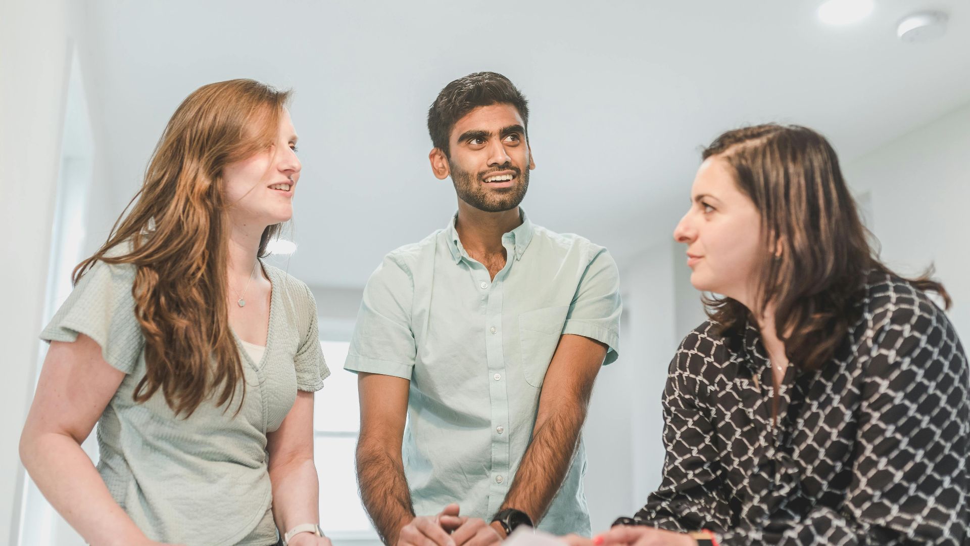 Three diverse adults conversing happily about real estate in a bright indoor setting.
