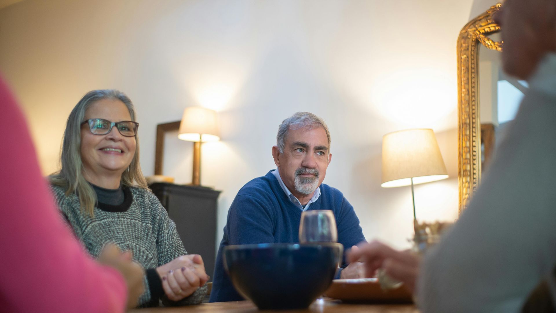 Senior couple smiling and talking at a cozy indoor setting, enjoying each other's company.