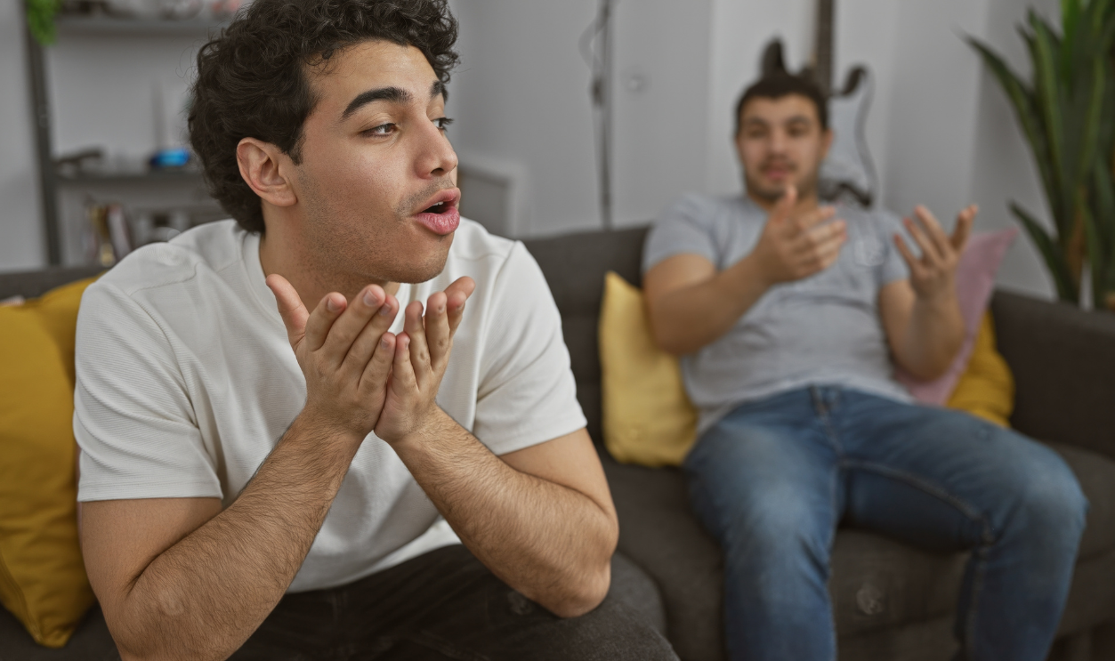 Two hispanic men having a lively discussion in a modern living room setting, expressing emotions and gestures.