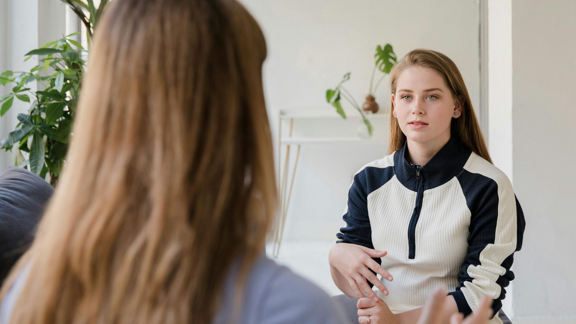 Two women talking in a bright, modern living room, sharing thoughts and gestures.
