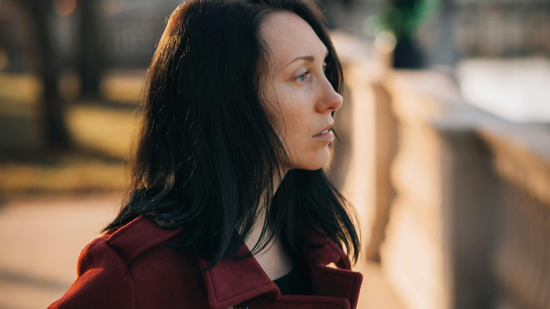 Woman in red coat gazing outdoors. Soft autumn light adds warmth and contemplation.