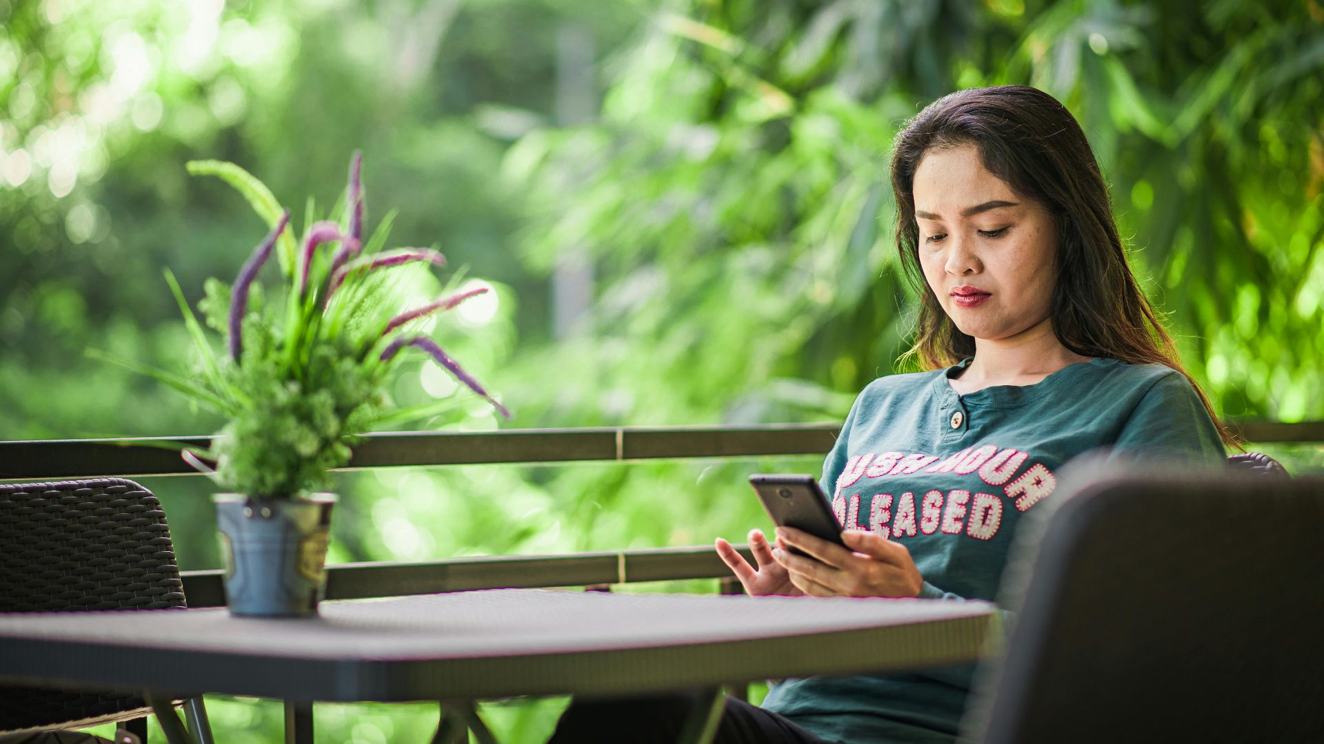 Concentrated young female freelancer browsing cellphone while working remotely in green outdoor terrace
